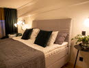 A bed with a gray fabric headboard. on a table next to it is a vase of flowers.