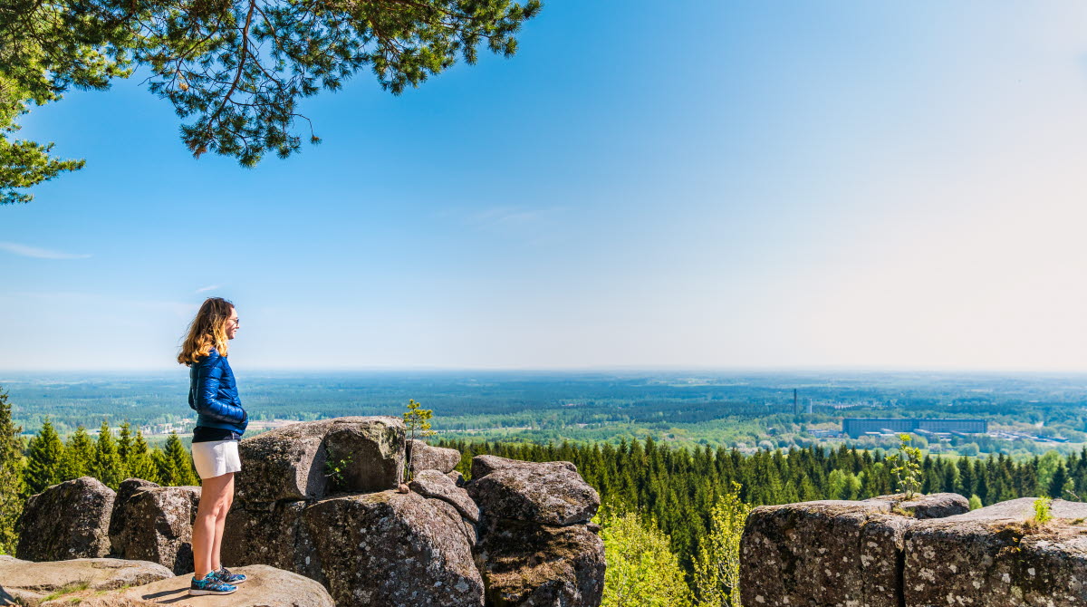 Ung kvinna står vid kanten av de stora diabaspelarna vid Ryds grottor och njuter av den blåa himmelen och den vackra utsikten.