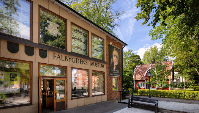 Exteriörbild på Falbygdens museum. Tegelbyggnad med stora fönster och en vepa med information om en utställning.