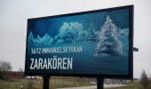 Stor digital skylt som står intill vägen visar reklam för Zarakörens konsert, mot en vintrigt landskap.