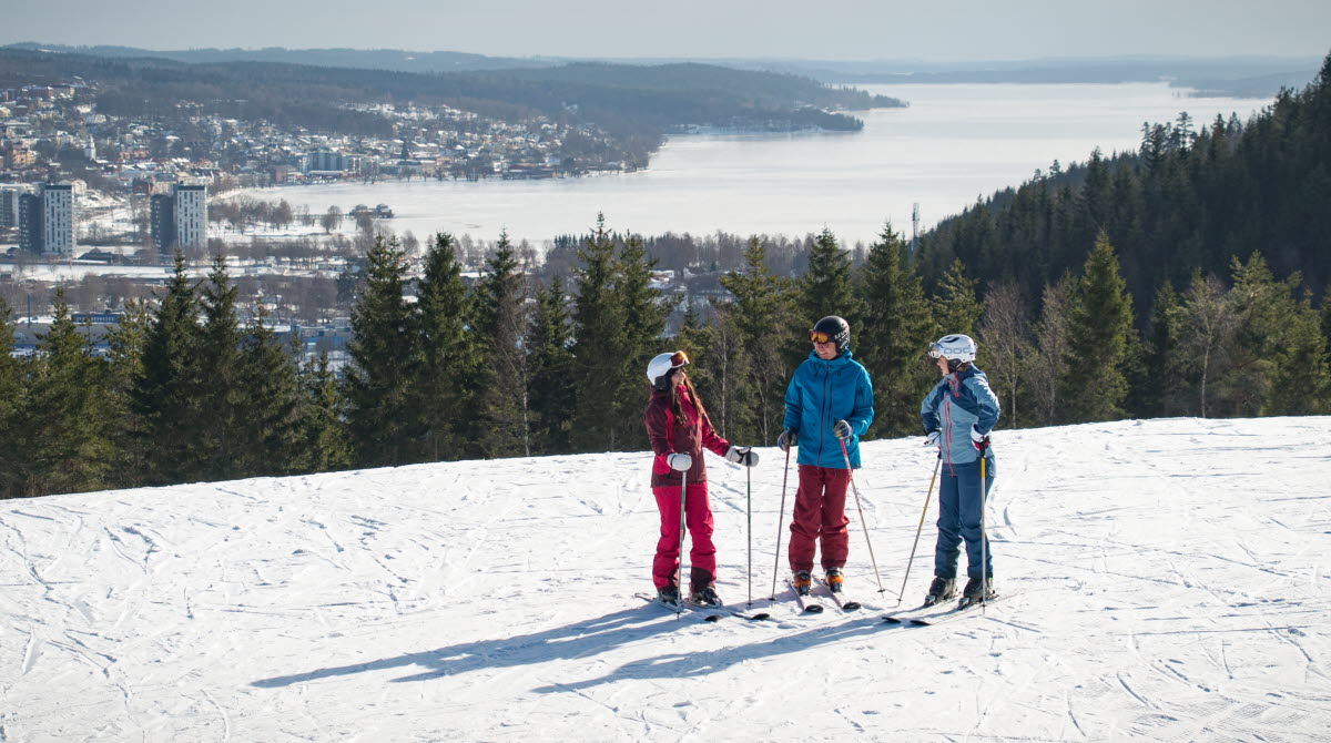 Tre barn i färgglada kläder på skidor på toppen av Ulricehamn Ski Center. 