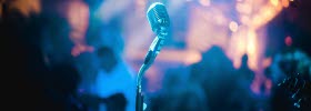 Microphone standing alone on stage, with people standing infront. 