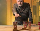 A man in uniform stands pointing towards the camera and a table with a map as its tabletop. Flag markers with the flags of the United Kingdom and Norway are scattered across the surface.