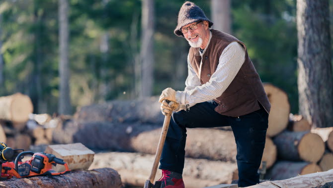 Man med yxa hugger timmer i skogen
