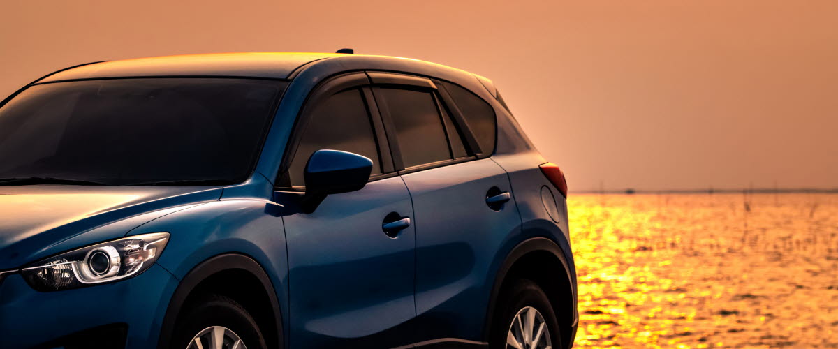 Car parked at concrete by sea at sunset