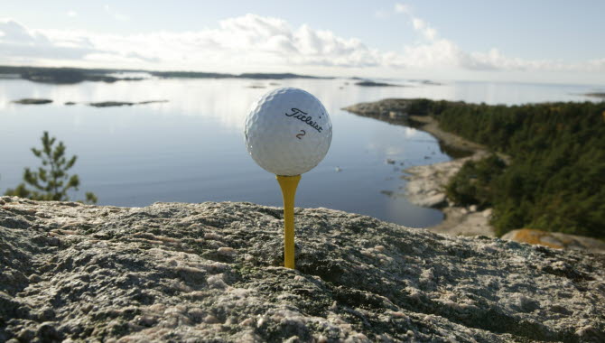 En golfboll placerad på en gul golfpeg, inkilad i ett berg. I bakgrunden syns Strömstads skärgård.