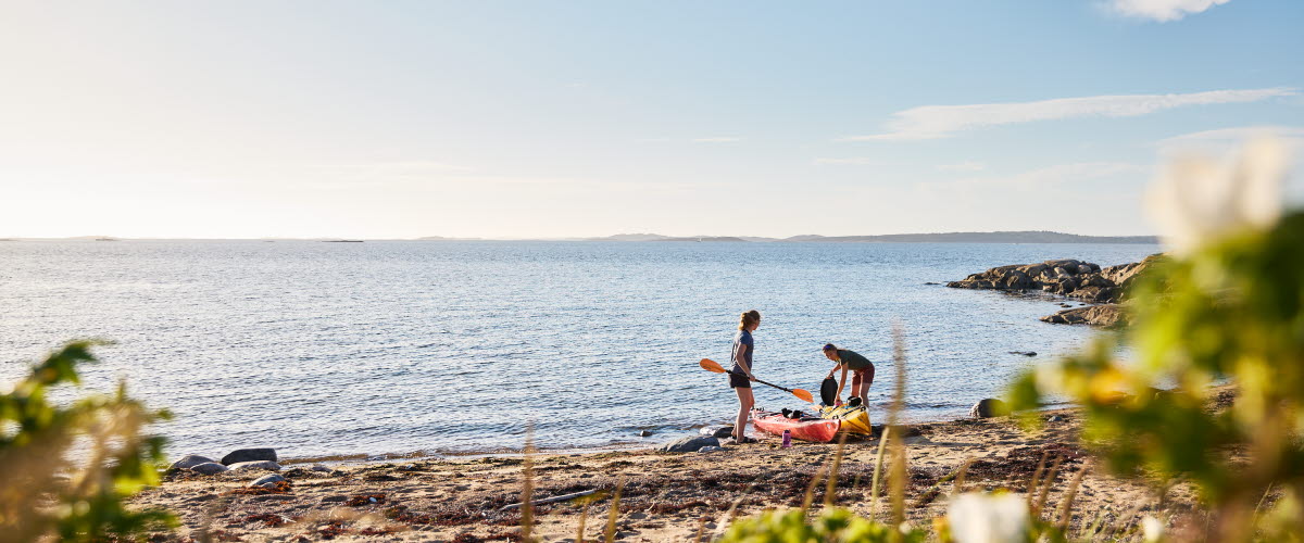 Två kvinnor drar upp sina kajaker på en strand.