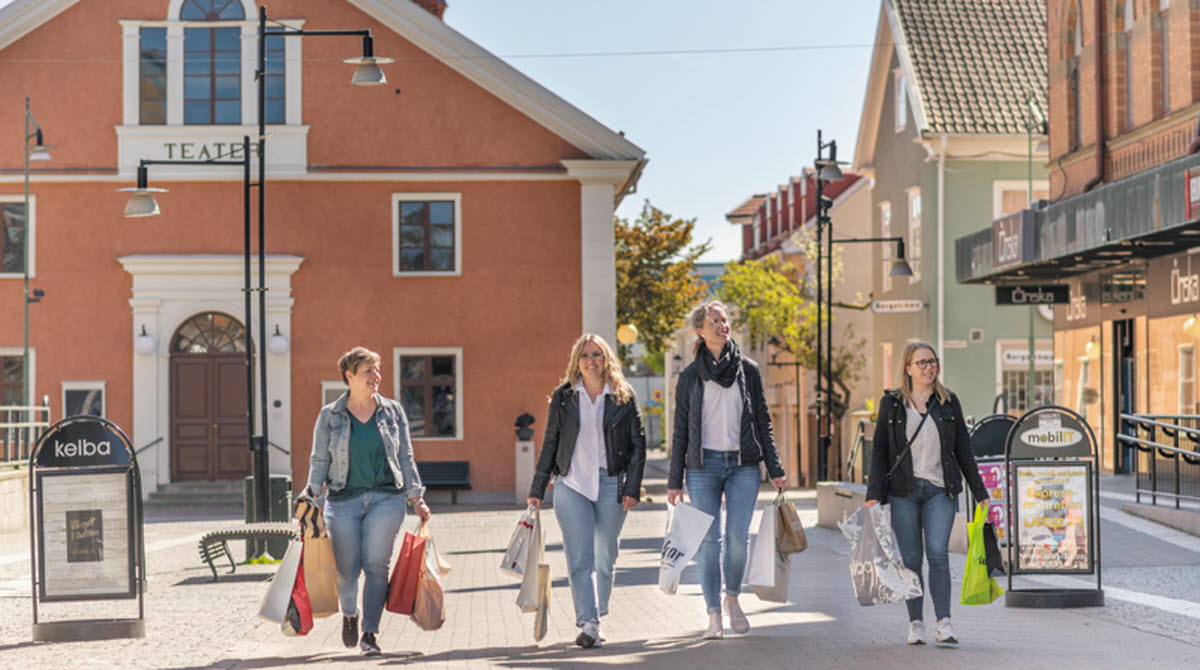 Fyra kvinnor går på gågatan i Mariestad. De har fyllda shoppingpåsar i händerna. 