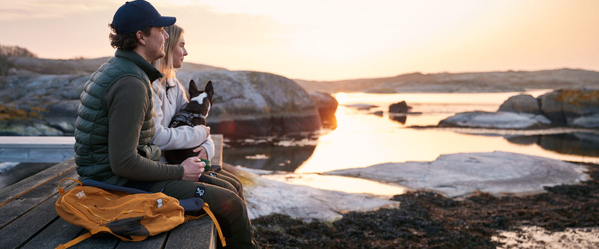 Två personer och en hund i kvällssolen.