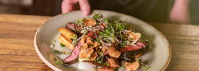 A hand holding up a plate of meat and vegetables.