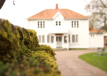 En vit äldre byggnad med många fönster. I förgrunden syns en mossbeklädd stenmur.