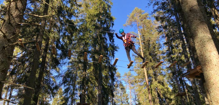 En person går på en bro av glest satta träplankor flera meter upp i luften i höghöjdsbanan på Billingen Skövde. 