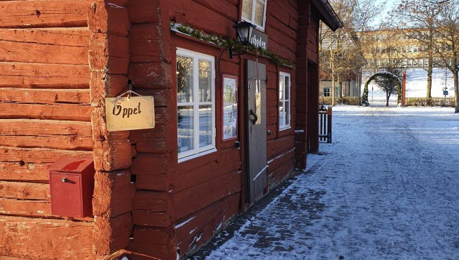The facade of a red cottage. On the corner there is a small wooden sign saying "Open".