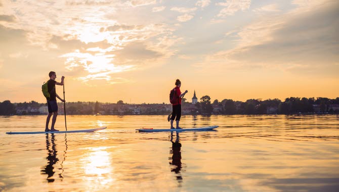 Två personer paddlar stand up paddling över en stilla Vättern i kvällssolen.