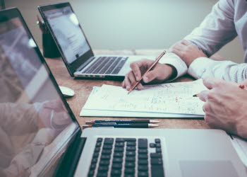 Två personer sitter framför två datorer i kontormiljö