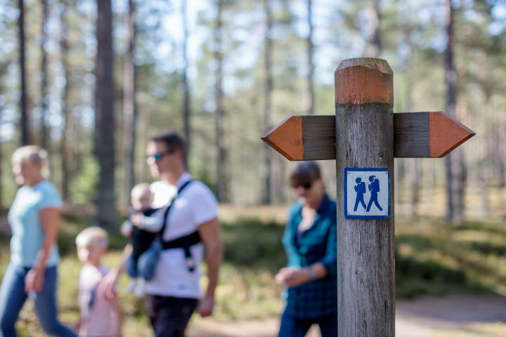A family walks on Hökensås nature reserve. A sign shows the road