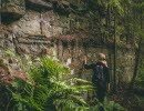 Woman standing by a mountain wall with her hand on the mountain.