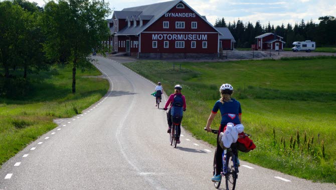 Personer cyklar på landsväg mot en stor röd byggnad