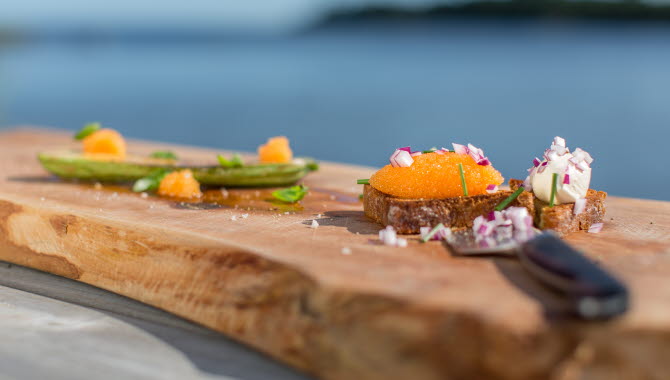 Brödskiva full av löjrom och finhackad rödlök serverad på en planka. Framför ligger en kniv.
