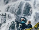 Two children sitting down and watching a waterfall