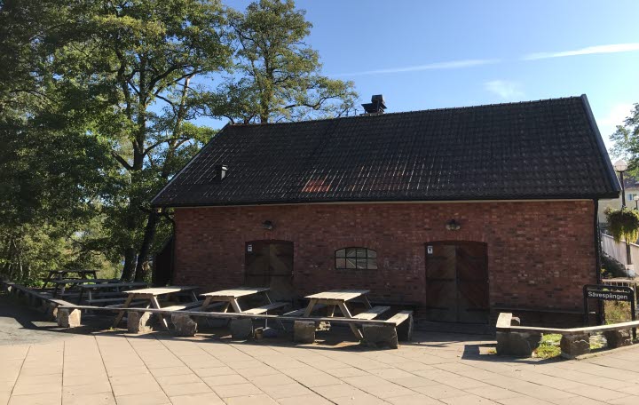 Röd tegelbyggnad med bänkar och bord framför.