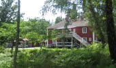 A red larger house with white knots, stairs and porches located in a lush area.