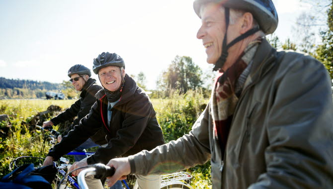 Tre män cyklar på rad ute på landsbygden.