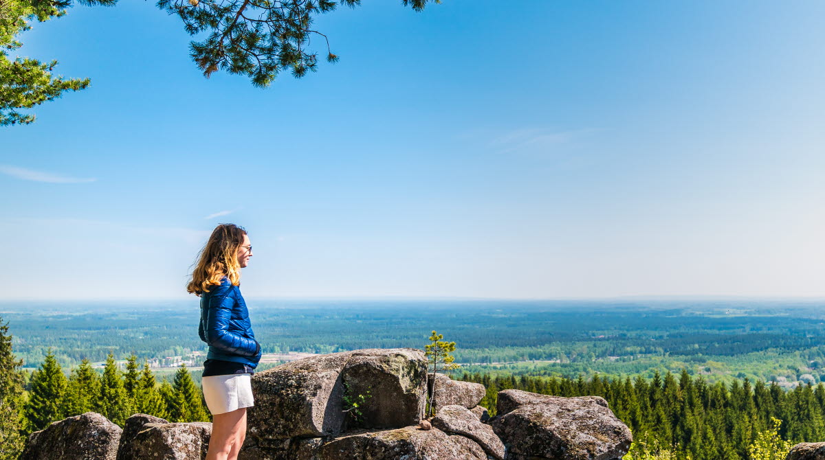 Ung kvinna står vid kanten av de stora diabaspelarna vid Ryds grottor och njuter av den blåa himmelen och den vackra utsikten. 