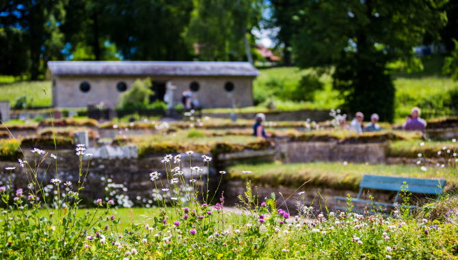 Människor står utomhus sommartid framför en tegelbyggnad med grönska runt omkring.