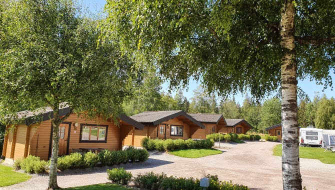 Timbered cottages next to each other, behind lush green trees at Billingens Stugby & Camping in Billingen Skövde.