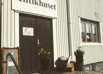En bild på två svartmålade dörrar på en ljusgrå husfasad. Ovanför dörren sitter en skylt där det står "Antikhuset".