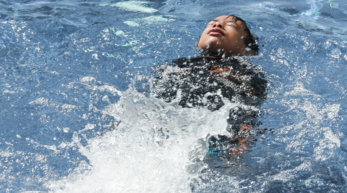 En bild på en liten pojke som ligger på rygg och flyter i en simbassäng.