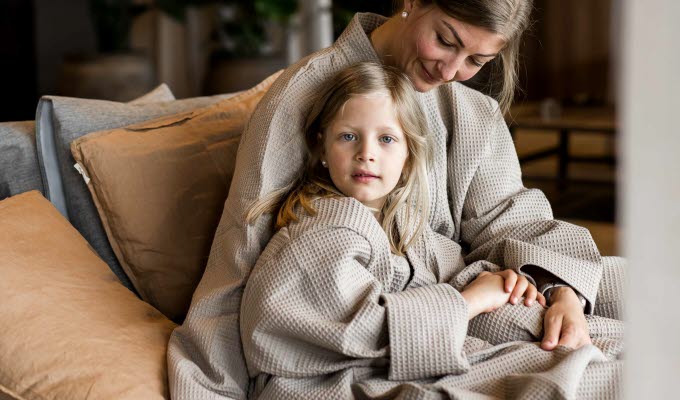 Kvinna och barn sittandes i en säng intill varandra, kvinnan tittar ner på barnet medan barnet kikar in i kameran.