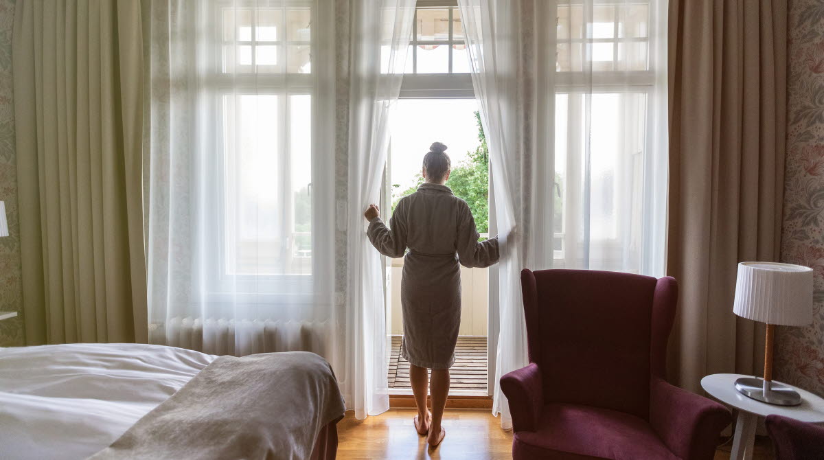 Kvinna i morgonrock står i dörröppningen till balkongen på hotellrummet.