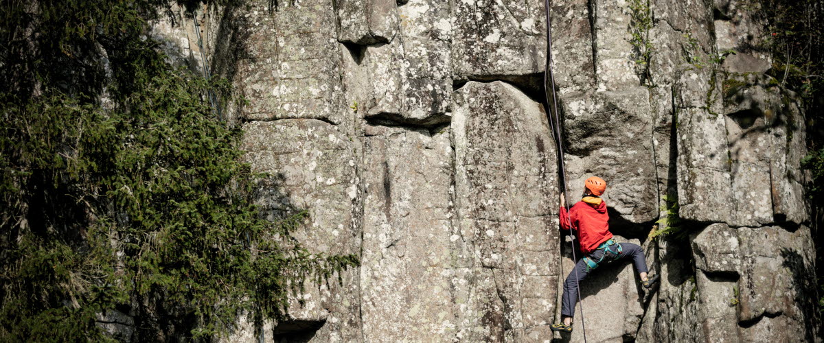 En kille i röd jacka som klättrar upp för en bergvägg. 