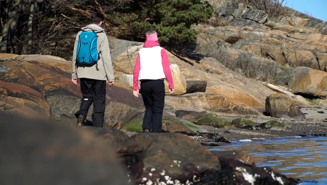Två personer vandrar längst en klippig strand på Nötholmen.