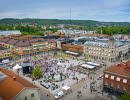 En flygbild på Hertig Johans torg i Skövde med många människor i rörelse. Runt torget syns byggnader.