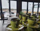 Green coffee cups in the foreground an set tables overlooking the lake.