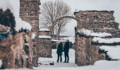 Snöigt landskap. Två personer står och kikar uppåt på en valvbåge i ruinerna av klosterkyrkan i Gudhem.