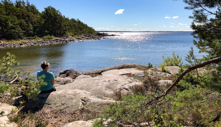 En kvinna sitter på en klippa och tittar ut över Vänerns vatten.