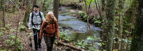 A man in plaid shirt and a women in a orange jacket is hiking