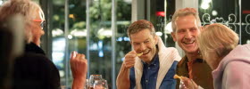 Two men and two women are eating on a restaurant, having a good time. 