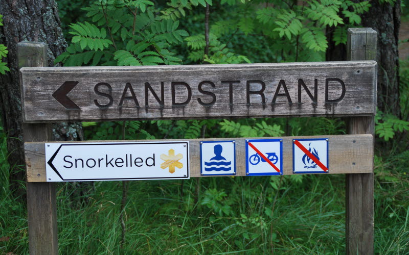 Träskylt som visar vägen till strand med snorkelled på ön Saltö