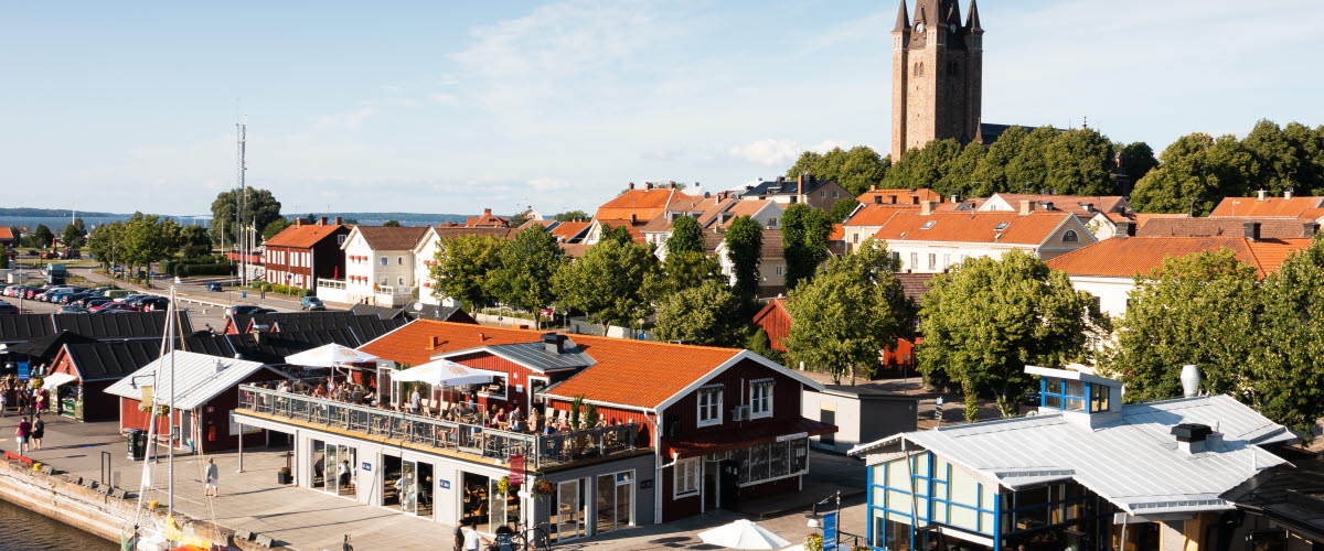 Flygfoto över Mariestads gästhamn med restauranger och bodar. I bakgrunden syns delar av Gamla Stan och Mariestads domkyrka.