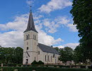 A white stone church with lush trees in front
