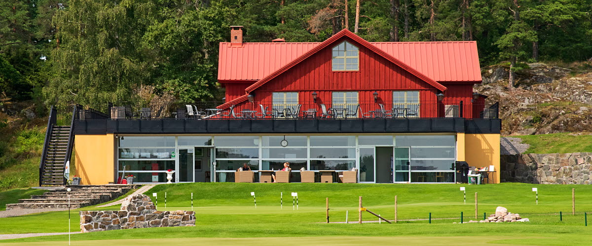 A red house with a green golf course in front
