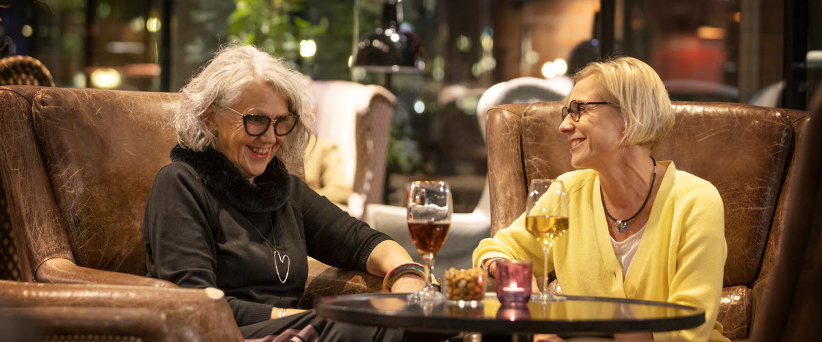 Two happy womens in brown chairs on a restaurant, drinking some wine. 