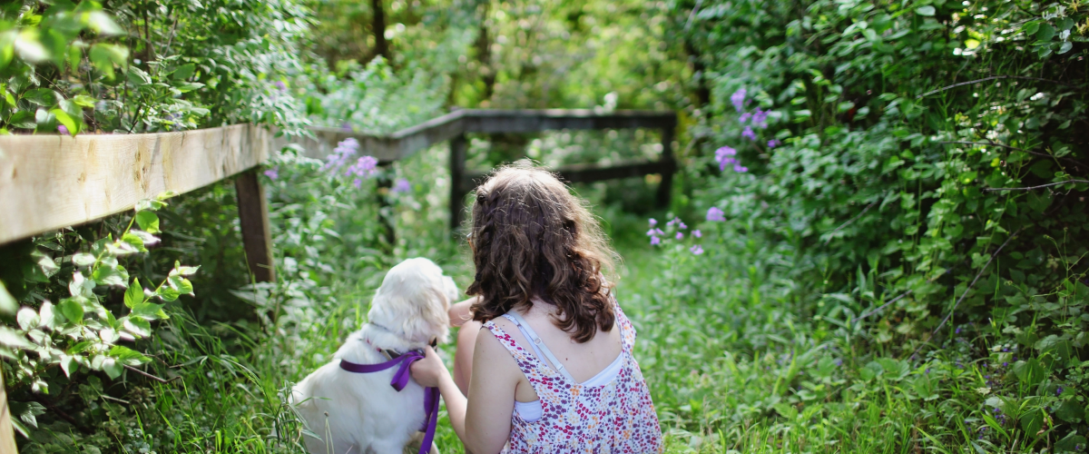 Hund och flicka sittandes i skogen.