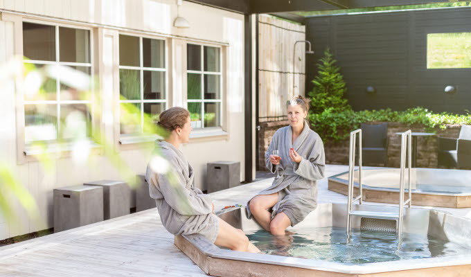 Två kvinnor som sitter med morgonrockar vid en utepool.