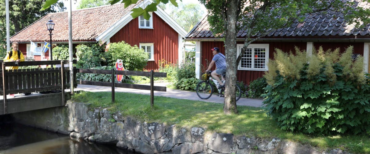 A person cycling on the path in front of Smedjestugorna on the Turbinhusön in Tidaholm on a summer day.